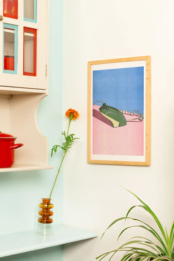 The KIBLIND Atelier Ana Popescu - Crusader Frog print adds color and style above a pastel wall and cream cabinet with red and blue accents, perfect for architecture and interiors lovers.