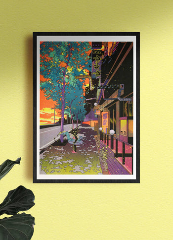 KIBLIND Ateliers Jinhwa Jang - Summer 1 framed artwork, featuring a neon-lit sunset street scene in Digital Media City, hangs on a light yellow wall with a green plant leaf in the corner.