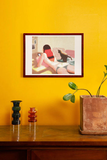 KIBLIND Ateliers Just Out Of The Bath by Saho Wajimaya hangs above a wooden table with glass decor and a potted plant, set against a bright yellow wall.
