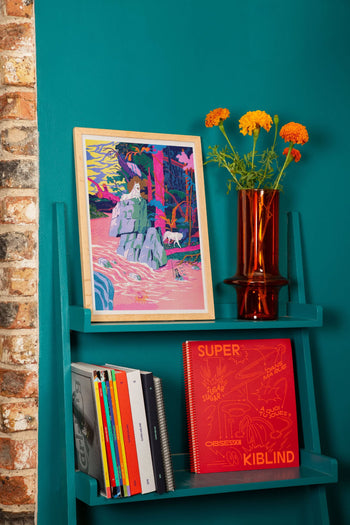 A teal wall features a shelf with colorful books, an orange vase of flowers, and KIBLIND Atelier’s Simon Roussin - Princess Mononoke artwork. Exposed brick appears on the left.