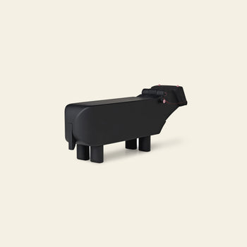 A minimalist black sculpture inspired by the Kay Bojesen Hippo from Kay Bojesen, featuring geometric body and legs, is set against a plain light beige background.
