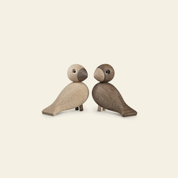 The Kay Bojesen Lovebirds Pair by Kay Bojesen features two minimalist wooden figures, crafted with Danish skill, sitting side by side against a light background, gently facing each other like lovebirds.