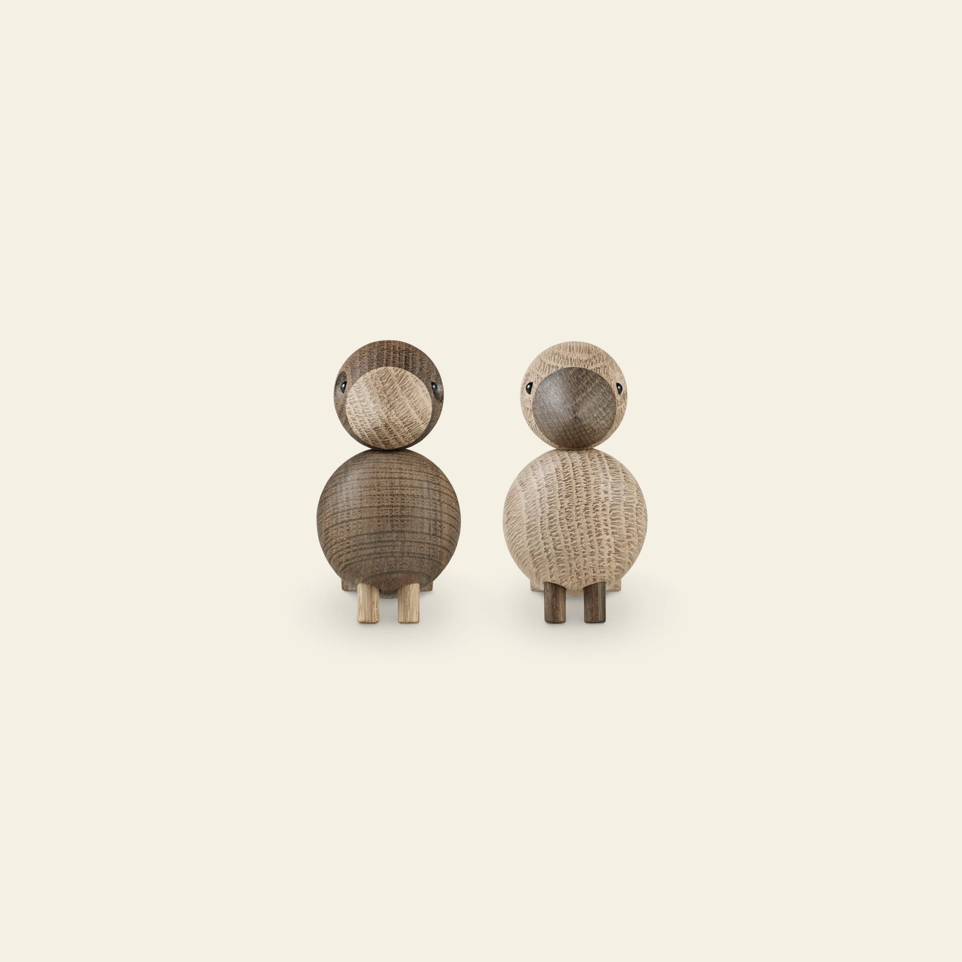 The Kay Bojesen Lovebirds Pair by Kay Bojesen features two wooden birds—one dark, one light—crafted with classic Danish design. Each has a simple rounded form and small legs, shown side by side on a plain, light background.