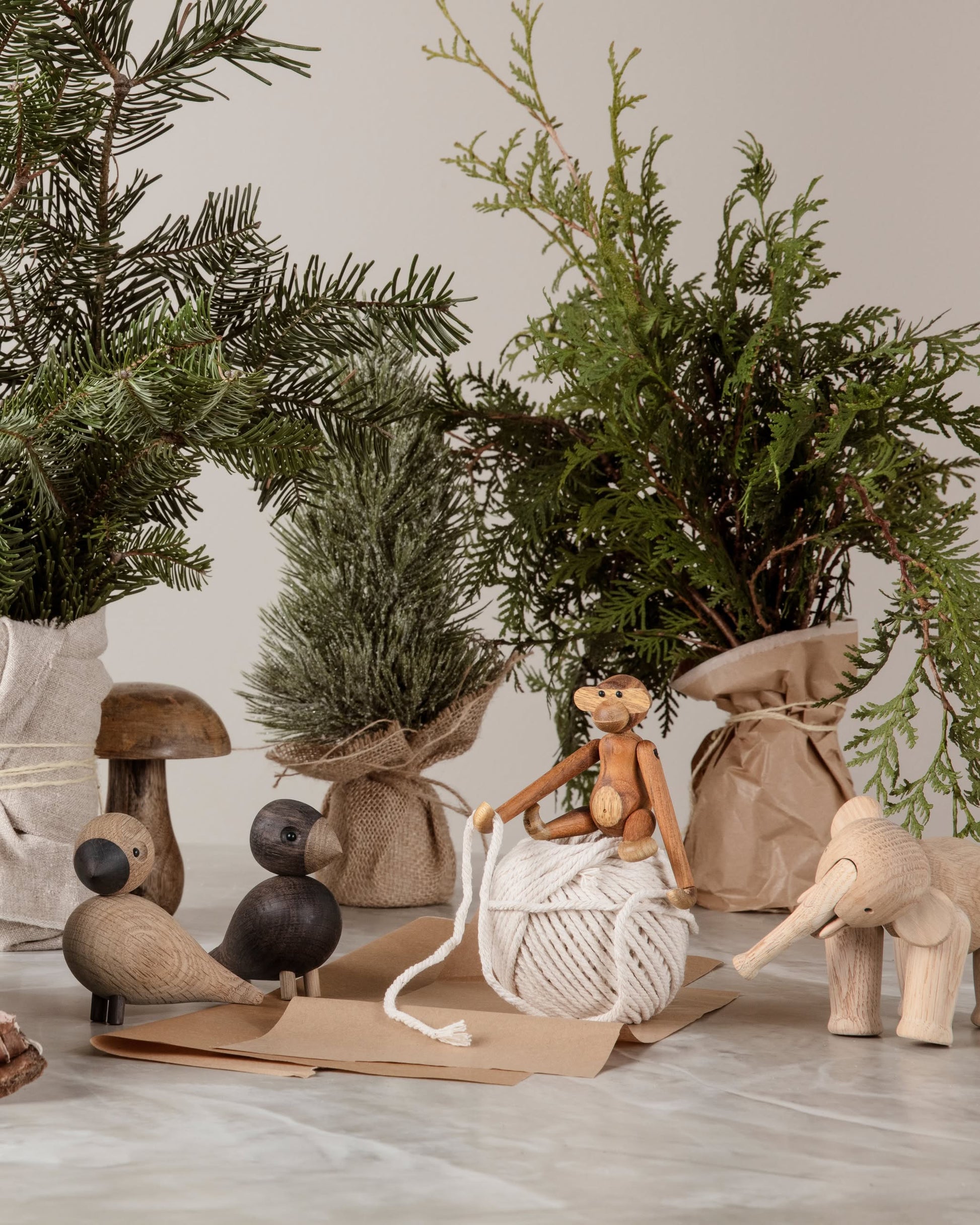 Kay Bojesen Lovebirds Pair by Kay Bojesen exemplifies Danish craftsmanship, displayed on a marble surface amidst white string, brown envelopes, and fabric-wrapped evergreen trees.