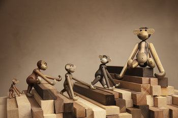 The Kay Bojesen Monkey Mini by Kay Bojesen poses playfully on stacked wooden blocks of different shades—an ideal collectible keepsake and design icon for any admirer.