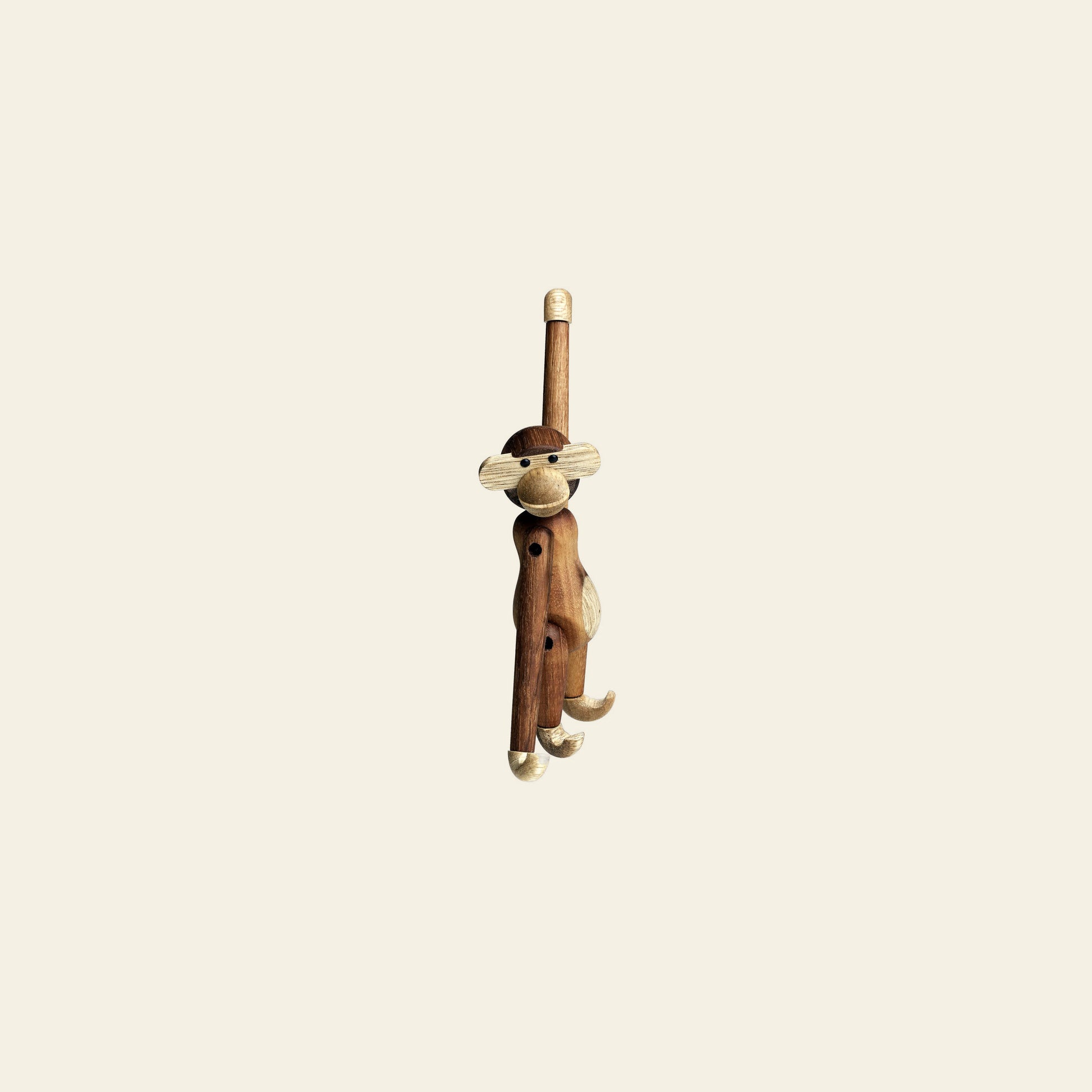 The Kay Bojesen Monkey Mini by Kay Bojesen, with movable limbs, hangs by one arm against a plain off-white background—a delightful collectible for design enthusiasts.