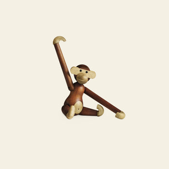 The Kay Bojesen Monkey Small by Kay Bojesen features movable limbs and sits on the ground, one arm raised and the other bent—this timeless design icon stands out against a plain light background.