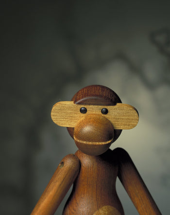 A close-up of the Kay Bojesen Monkey Small by Kay Bojesen—a design icon with round eyes and flat, oval ears—set against a blurred background.