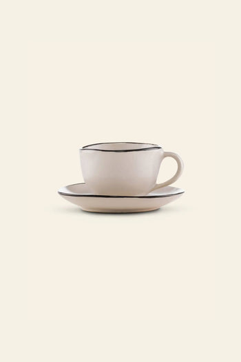 The Kra Sanctuary Andaman Free-Form Cup with handle and matching coaster features an off-white finish with thin, dark rims, bringing relaxed island elegance to your diningware. Shown on a plain, light background.