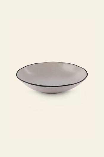 The Kra Sanctuary Andaman Free-Form Pasta Bowl is a shallow, round beige ceramic bowl with a slightly irregular rim and dark edge, hand-painted glaze, showcased against a plain light backdrop.