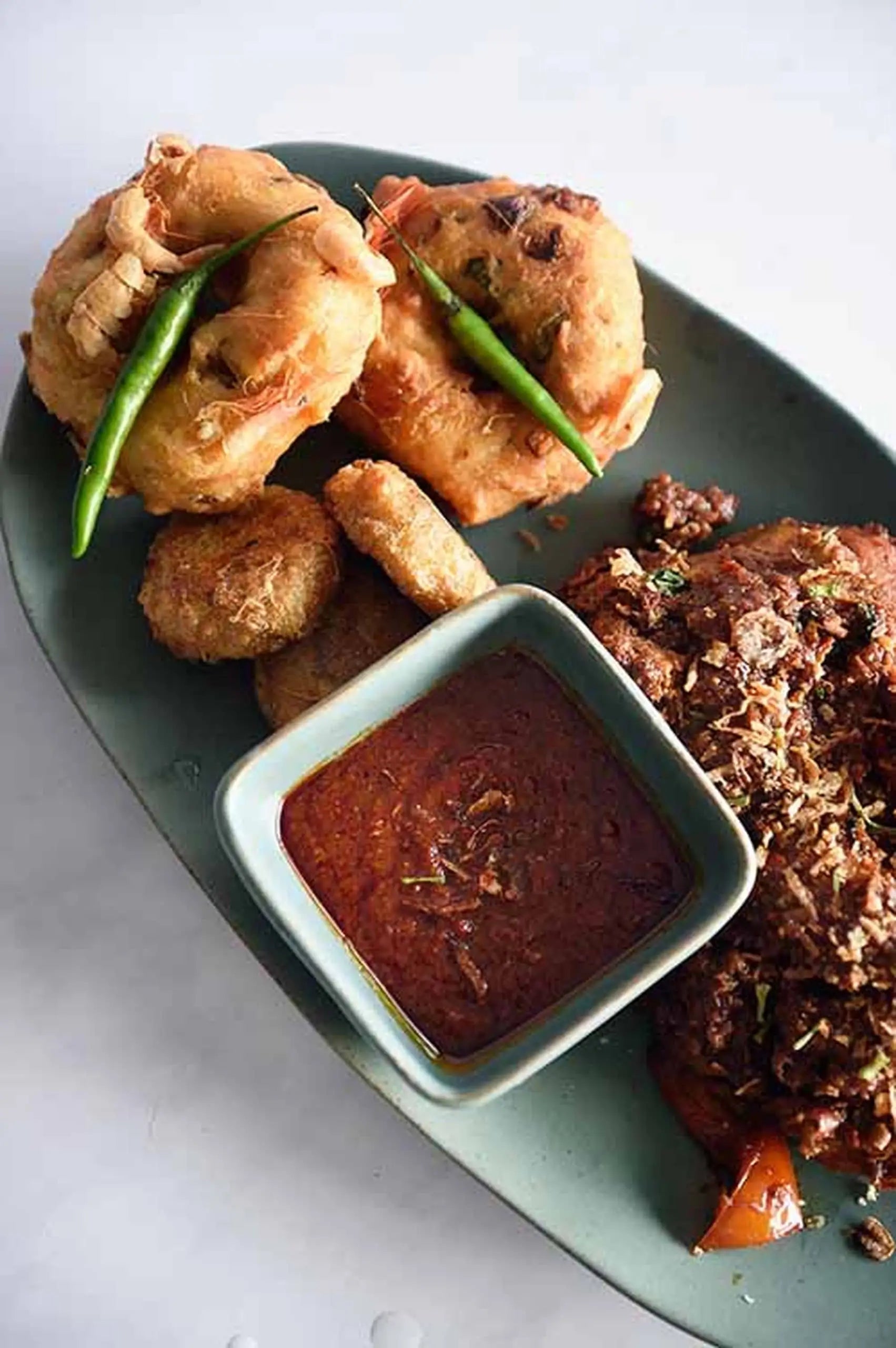 A Kra Sanctuary Karst Square Snack Bowl holds fried snacks, a spicy meat dish, and red sauce, garnished with green chilies on the left. Presented against a light background, this setup creates a distinctive look.