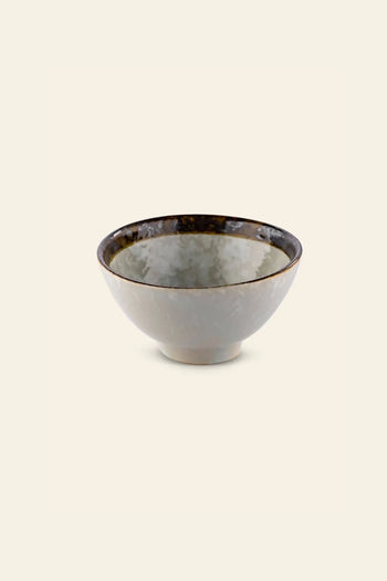 The Kra Sanctuary Satay Everyday Rice Bowl by Kra Sanctuary features a glossy, marbled gray exterior with a dark brown rim, creating an earthy look thats beautifully showcased against a plain, light beige background.