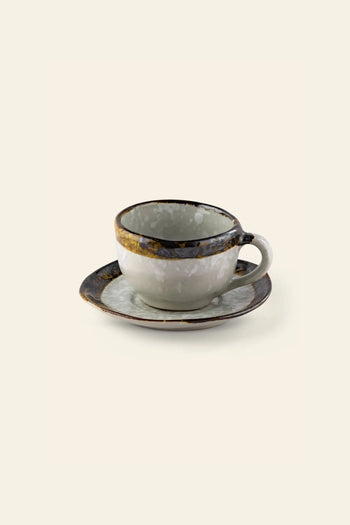 The Kra Sanctuary Satay Free-Form Cup and Coaster features a handle, mottled dark and light glaze, and an iridescent border—perfect against a plain background to enhance your earthy dinnerware collection.