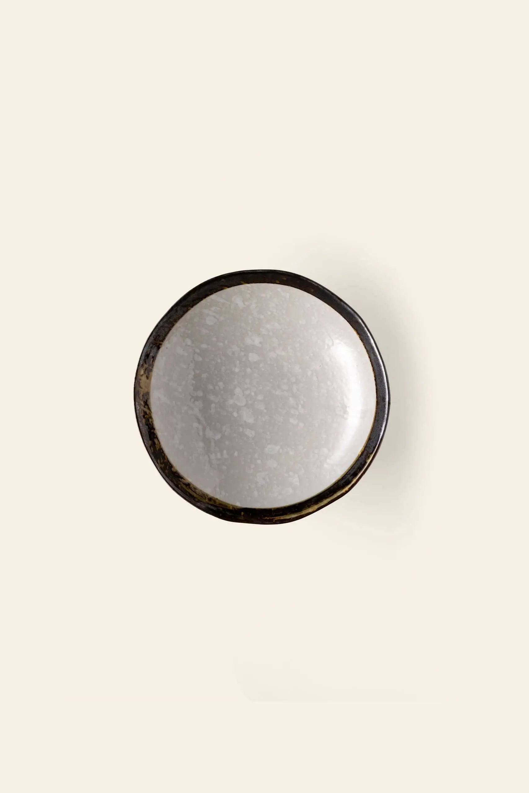 The Kra Sanctuary Satay Free-Form Pasta Bowl by Kra Sanctuary features a round, shallow design with a dark, uneven rim and light speckled interior—photographed from above on an off-white background—ideal for elevating your dining experience.