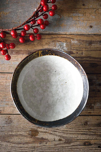 The Kra Sanctuary Satay Free-Form Soup Bowl, featuring a light, textured interior, rests on a weathered wooden table beside a decorative branch of red berries.