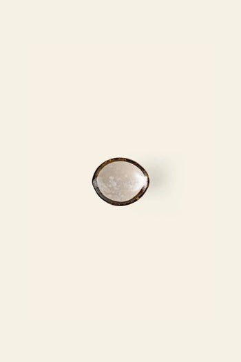 The Kra Sanctuary Satay Shell Dipping Dish by Kra Sanctuary, featuring a gently textured surface and an iridescent edge, is centered on a plain, off-white background.
