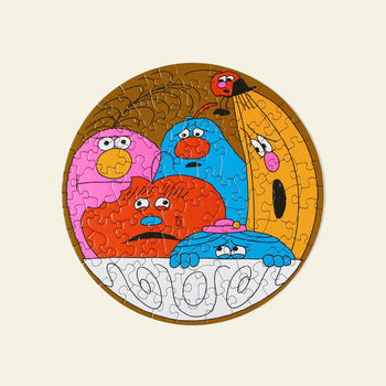Le Puzz’s A Fruity Fiasco 81-piece round puzzle features colorful, cartoonish pink, blue, red, and yellow characters with expressive faces huddled together in a fruit bowl for a playful scene.