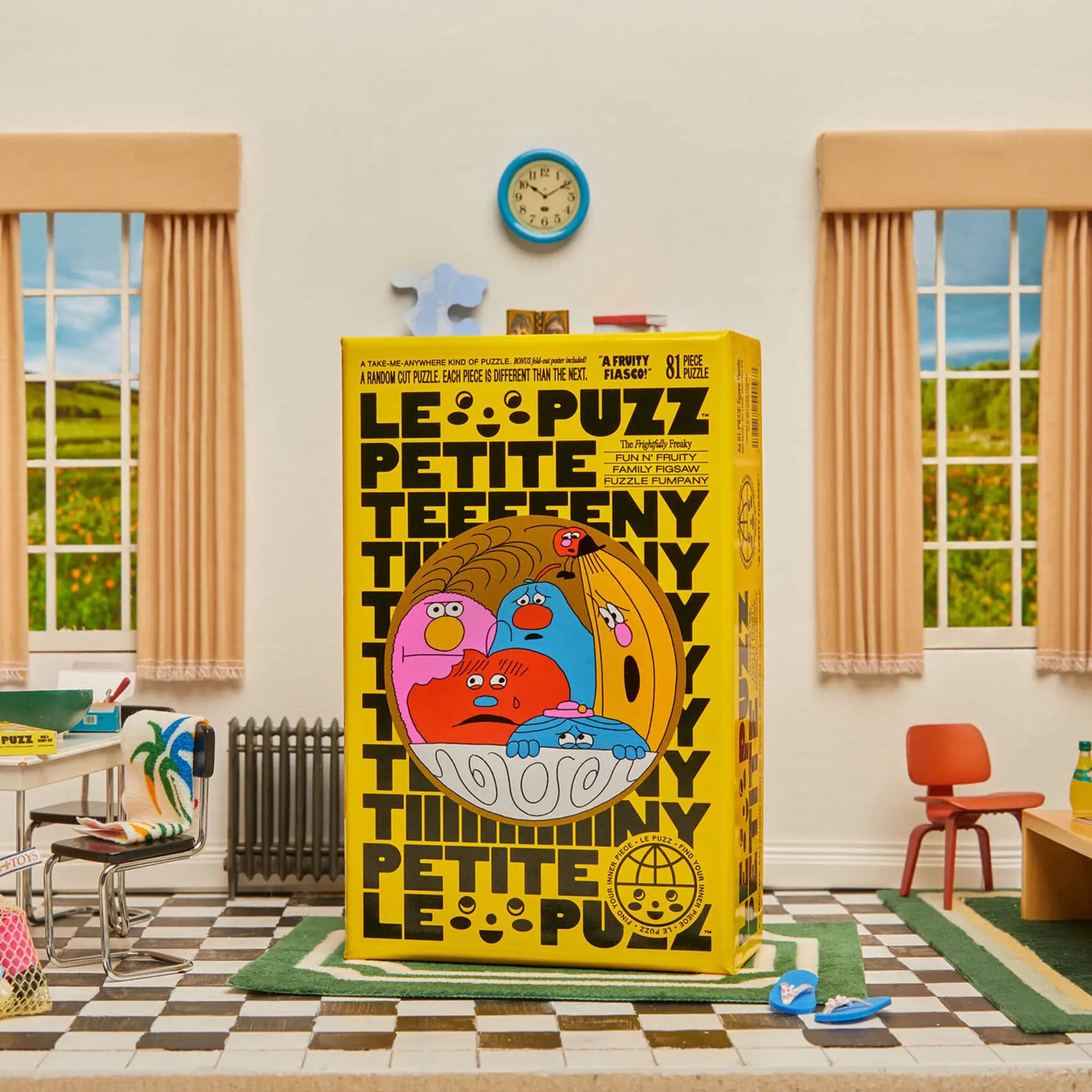 Le Puzzs A Fruity Fiasco 81-piece puzzle box, featuring bold black text and a colorful fruit bowl, is displayed at the center of a retro room with two windows, a clock, beige curtains, and classroom furniture.