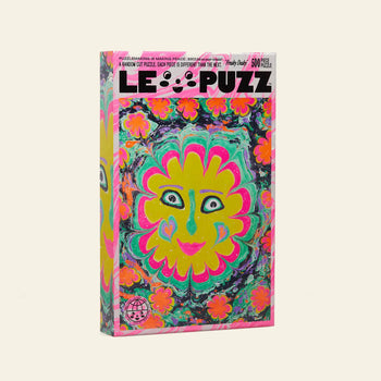Le Puzz Freaky Deaky, a 500-piece puzzle by Le Puzz, features a vibrant floral design with a large smiling yellow and pink sun-like face surrounded by orange and green flowers.