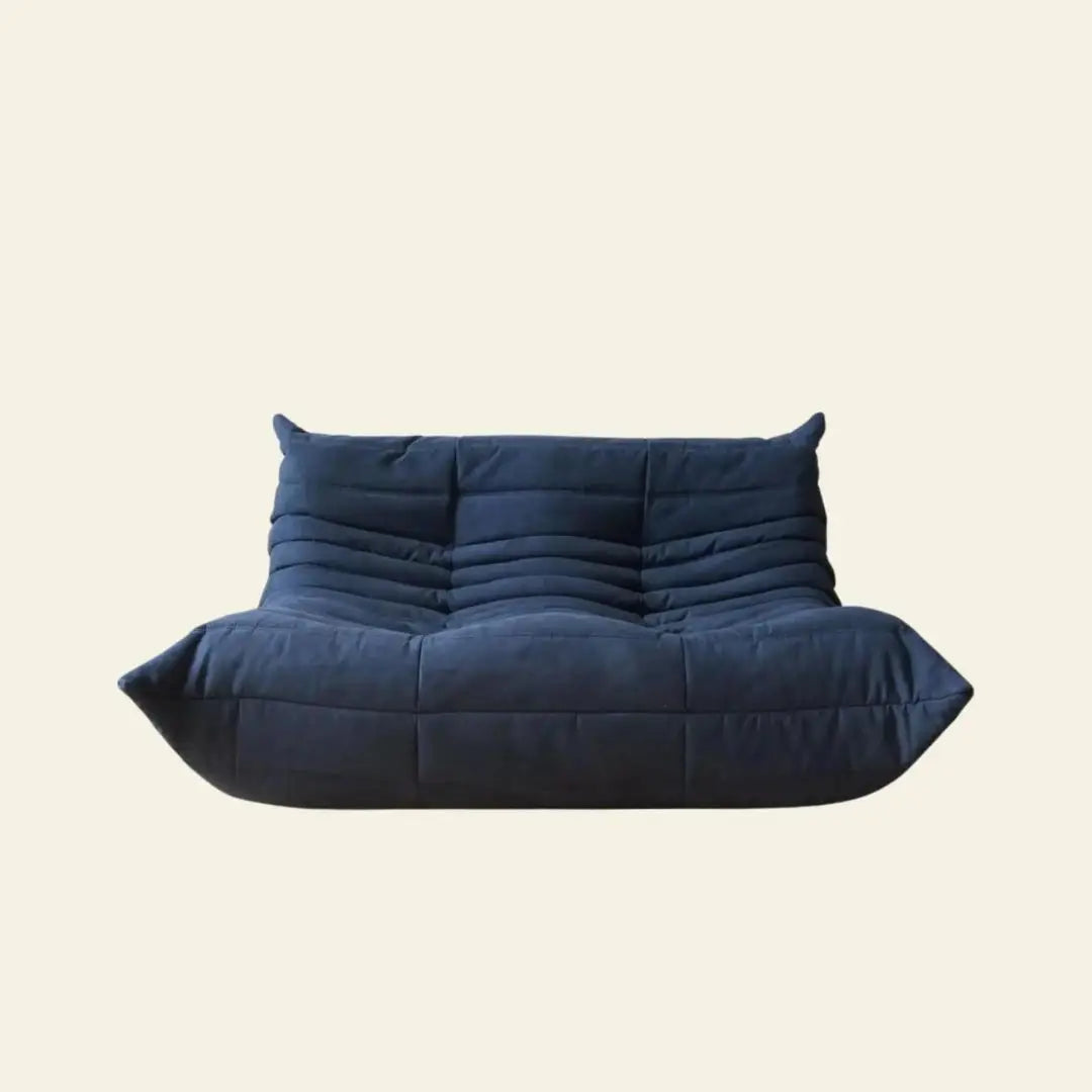 The Ligne Roset Togo 2 Seater by Ligne Roset is a modern, low-profile navy blue sofa with quilted cushions and soft, rounded edges, inspired by mid-century design, shown against a plain off-white background.