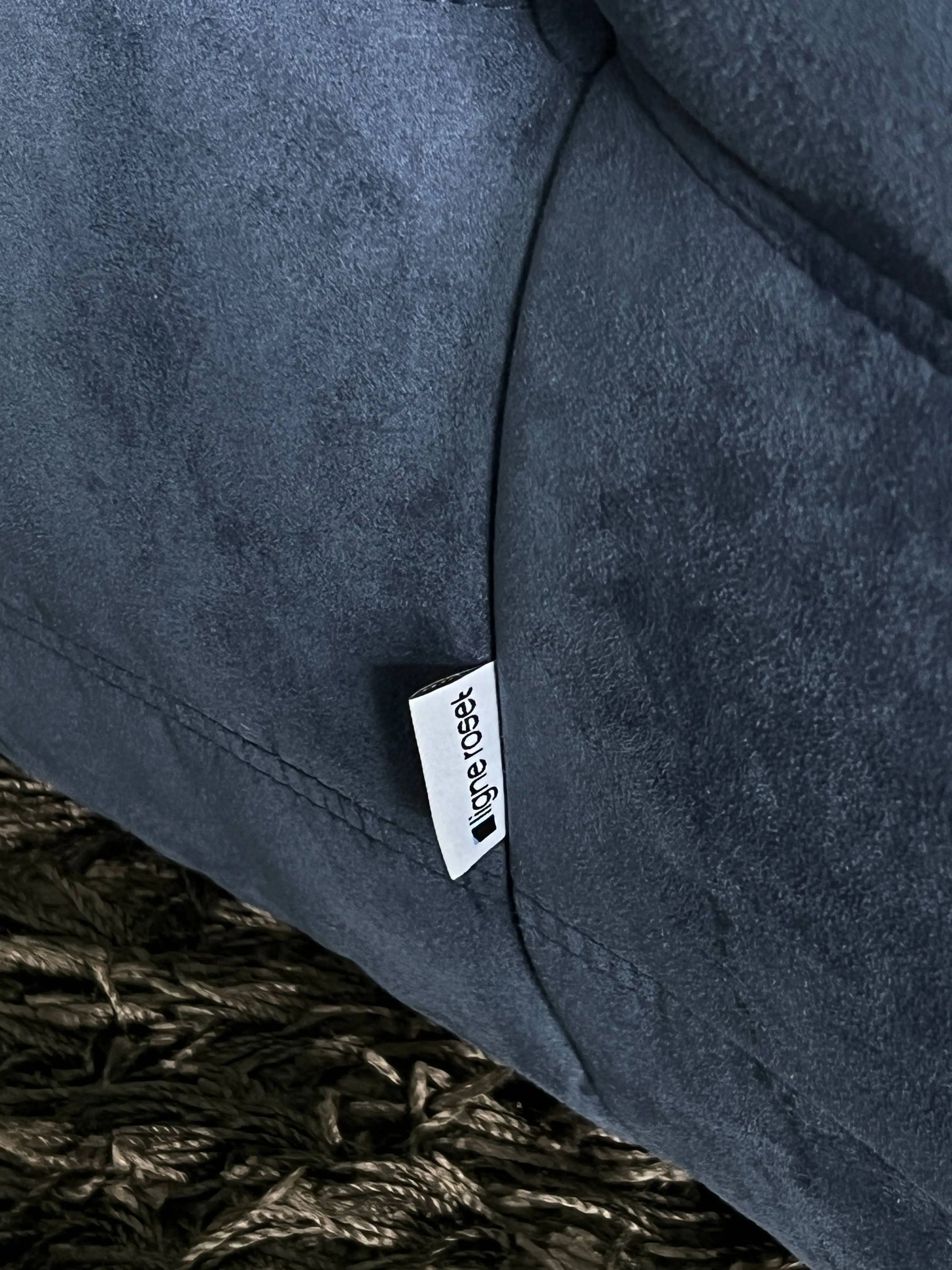 A close-up of the dark gray Ligne Roset Togo 2 Seater, inspired by mid-century design, featuring a white fabric tag and resting on a dark woven rug.