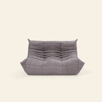The Ligne Roset Togo, 2 Seater by Ligne Roset is a modern, low-profile gray sofa with a quilted, tufted design and deep cushioned seat and backrest, inspired by mid-century style—ideal against a plain light background.