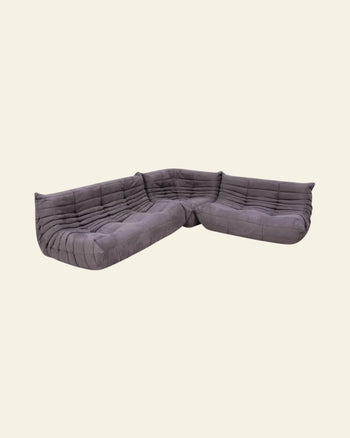 The Ligne Roset Togo, 2 Seater by Ligne Roset is a modern gray fabric sofa with low-profile tufted upholstery and modular design, evoking a relaxed vibe against a plain cream background.