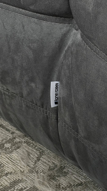 A close-up of gray suede-like fabric with visible stitching and a small white tag, highlighting the modular design of the Ligne Roset Togo, 2 Seater by Ligne Roset, inspired by iconic mid-century sofas.