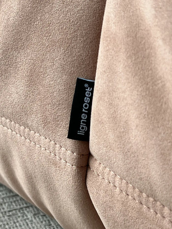 A close-up of beige suede-like fabric with visible stitching and a small black “ligne roset®” tag highlights the iconic pleated design of the Ligne Roset Togo, 3 Seater sofa.