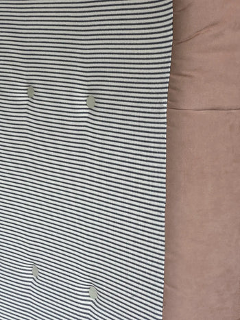 Close-up of the Ligne Roset Togo, 3 Seater by Ligne Roset: thin black and white horizontal stripes with four round buttons beside a smooth, light brown pleated fabric section on the right.