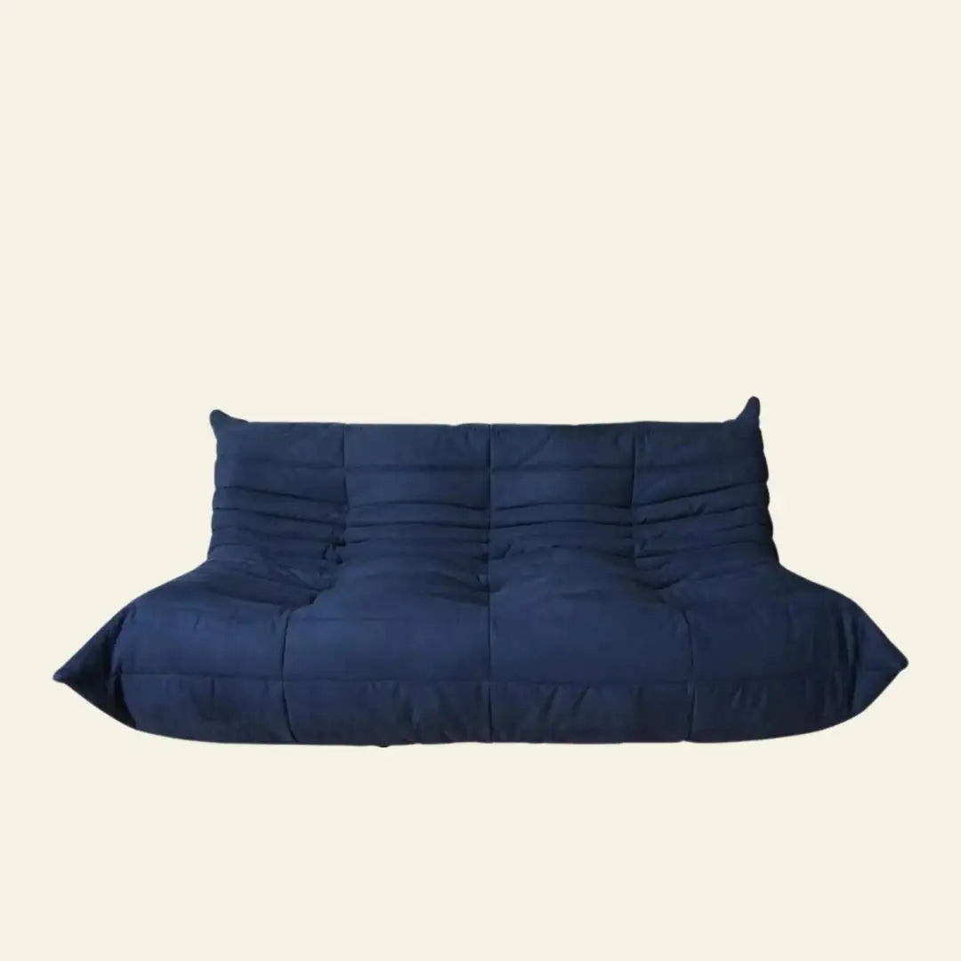 The Ligne Roset Togo 3 Seater by Ligne Roset is a modern, deep blue, armless sofa with a quilted, tufted design and low profile, inspired by mid-century style and set against a plain light beige background.