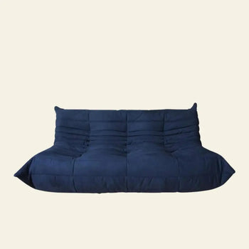 The Ligne Roset Togo 3 Seater by Ligne Roset is a modern, deep blue, armless sofa with a quilted, tufted design and low profile, inspired by mid-century style and set against a plain light beige background.