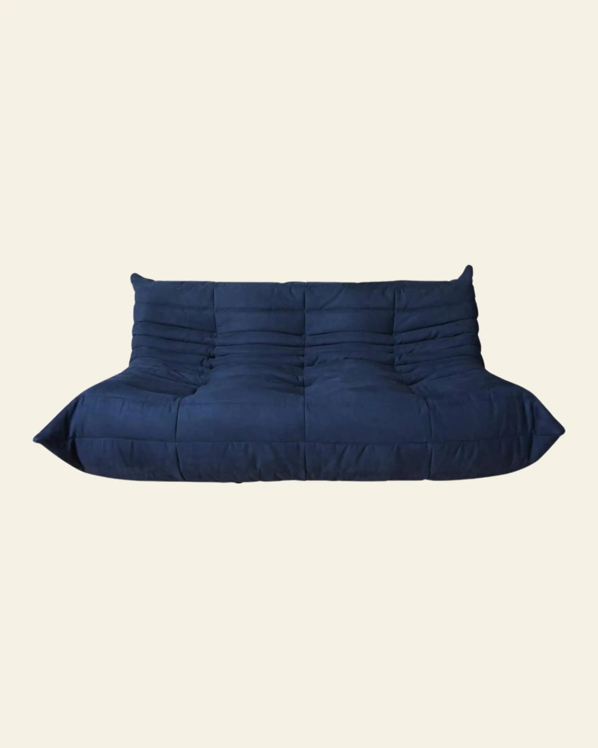 The Ligne Roset Togo 3 Seater by Ligne Roset is a modern, deep blue, low-profile sofa with plush tufting and softly sloped arms inspired by mid-century design, shown against a plain off-white background.