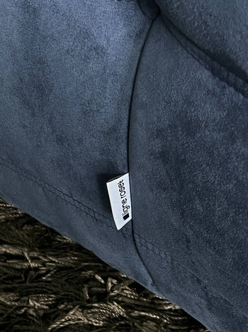 A close-up of the Ligne Roset Togo, 3 Seater by Ligne Roset in dark gray fabric with a white label, resting on a textured dark brown rug—an inviting accent inspired by modular mid-century design.