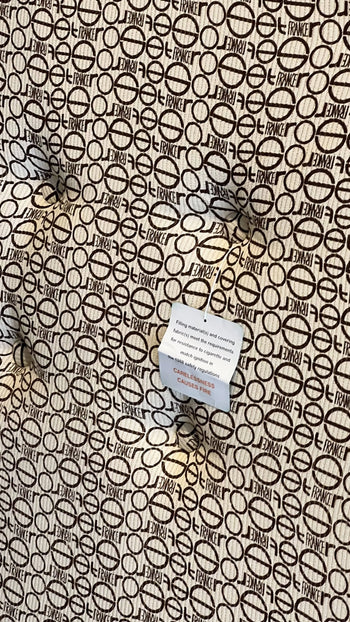 The Ligne Roset Togo 3 Seater by Ligne Roset features a tufted surface with a repeating circular pattern and “FRANCE” text, echoing mid-century design. A white care label with red text and instructions is also attached.