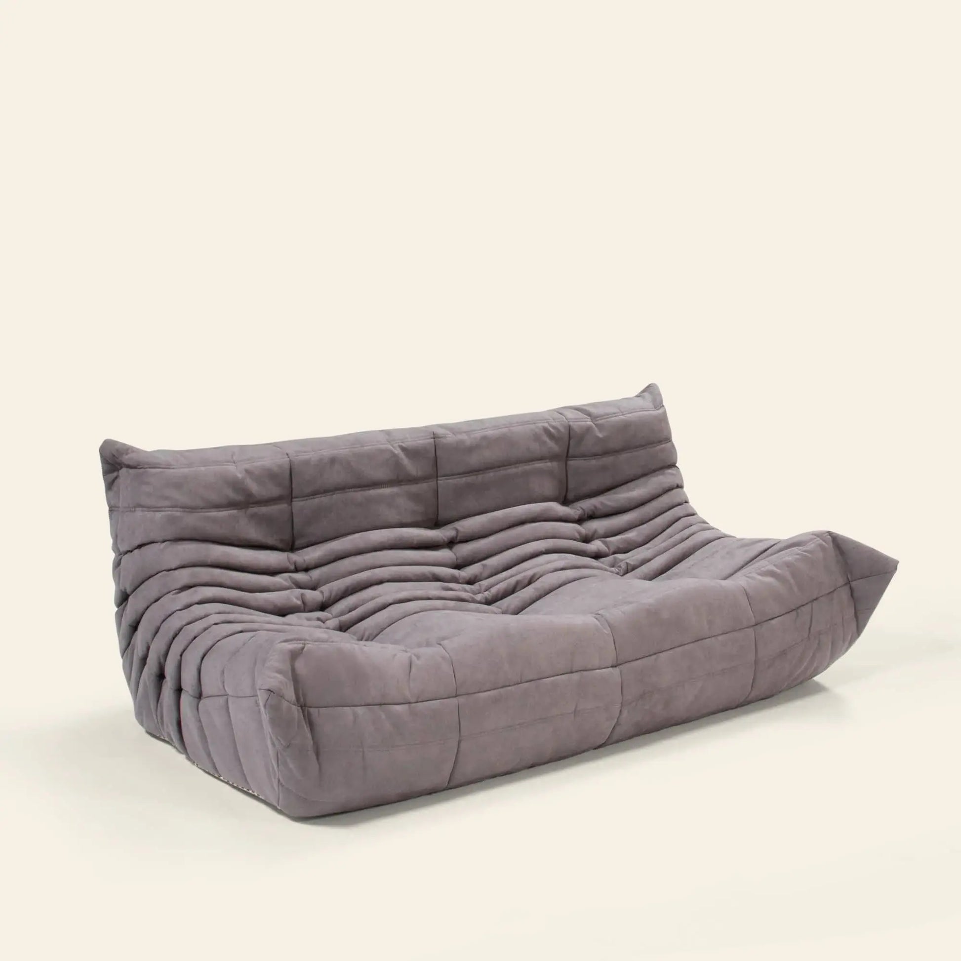 The Ligne Roset Togo 3 Seater by Ligne Roset is a modern, low-profile gray sofa with a tufted, quilted design and no visible legs, styled against a plain off-white background.