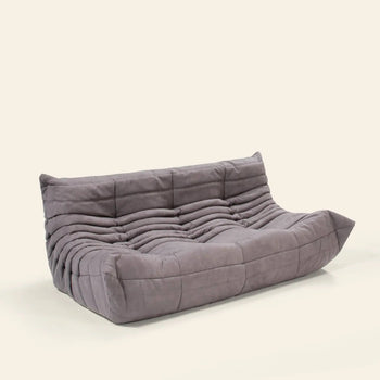 The Ligne Roset Togo 3 Seater by Ligne Roset is a modern, low-profile gray sofa with a tufted, quilted design and no visible legs, styled against a plain off-white background.