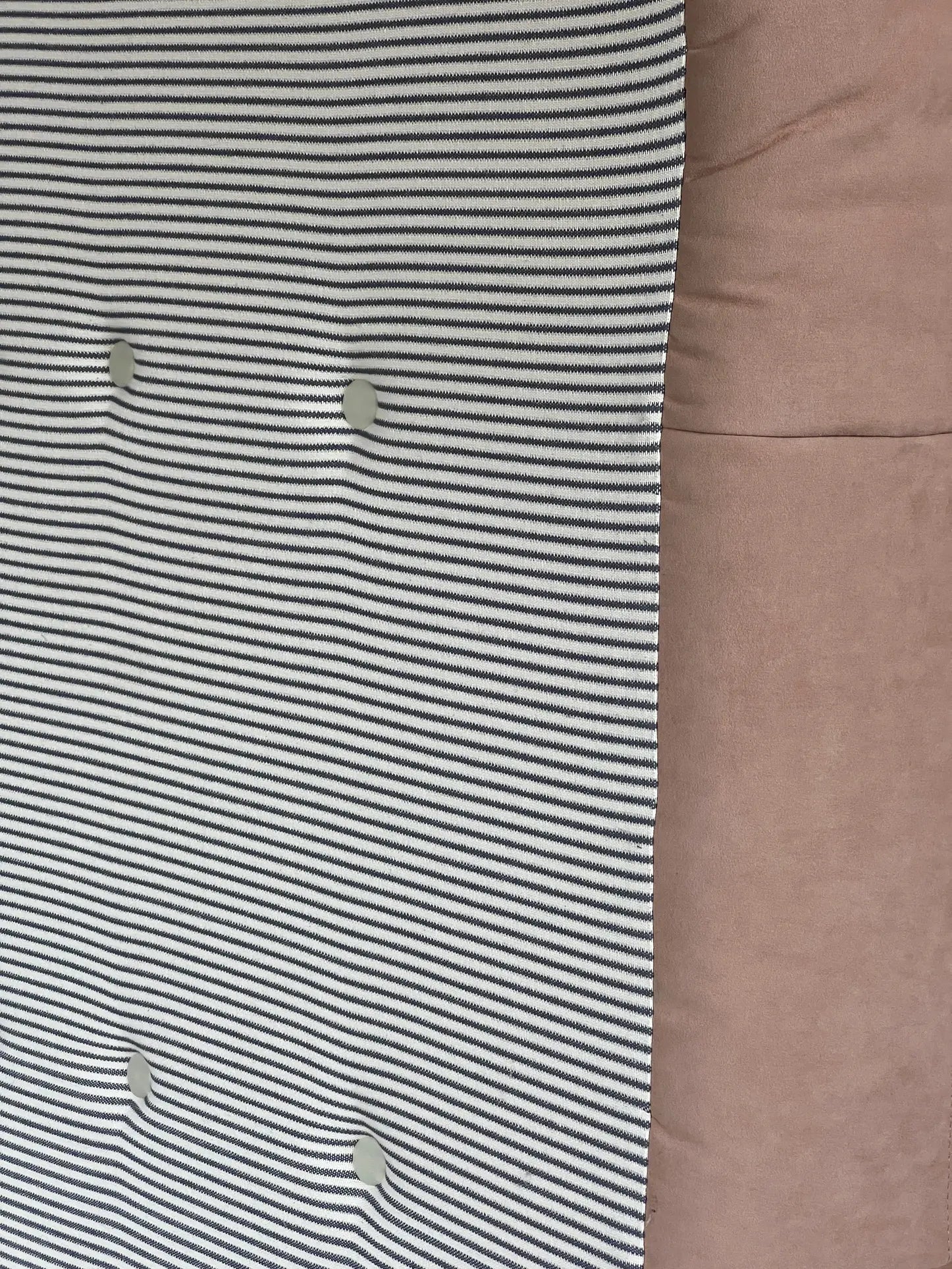 A close-up of the Ligne Roset Togo Corner Seat by Ligne Roset, featuring black and white horizontal stripes with four round buttons, alongside light brown fabric on the right.