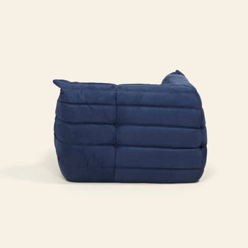 The Ligne Roset Togo Corner Seat by Ligne Roset is a modern, deep blue chair with a low back and pleated segmented cushioning, shown from the side against a plain light background.