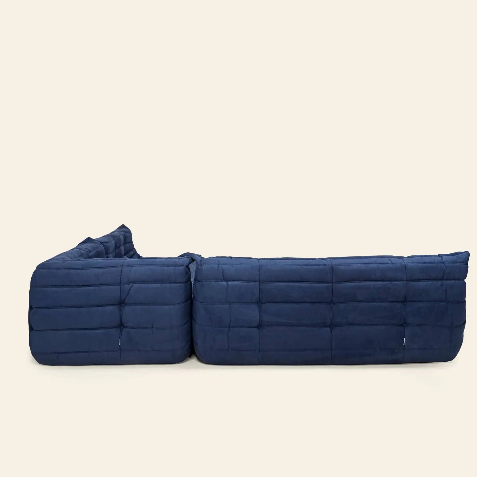 The Ligne Roset Togo Corner Seat by Ligne Roset features deep blue pleated fabric and a quilted, padded finish, shown from the back against a plain beige background.