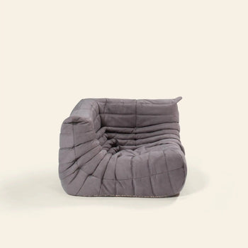 The Ligne Roset Togo Corner Seat by Ligne Roset features a modern, low-profile armless design with soft, tufted gray upholstery and a plush, segmented look, inspired by mid-century modular style.