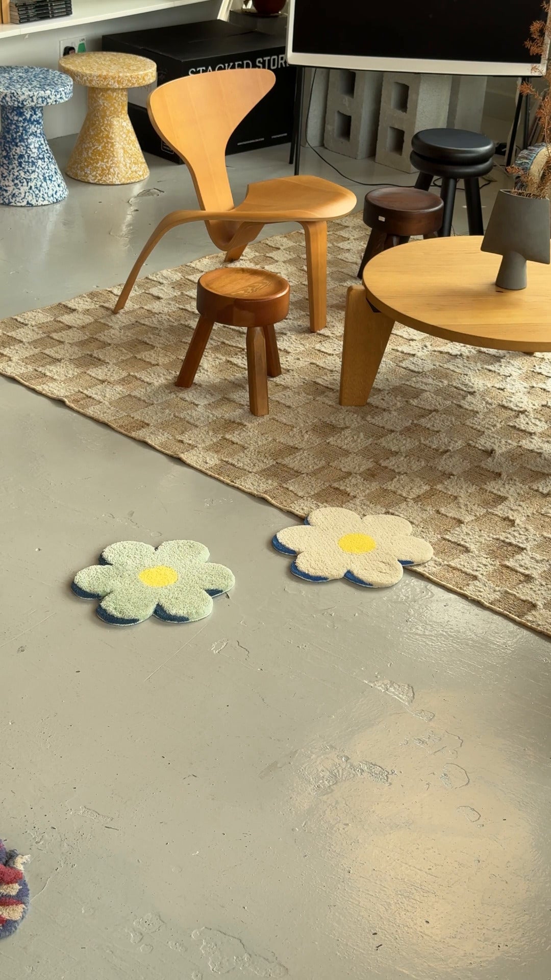 A modern room with wood furniture, a patterned rug, and two MIYOSHI RUG Flower Chair Rug C pieces on a gray floor. The cozy, minimalist space features neutral and pastel hues and showcases MIYOSHI RUGs handcraftsmanship.