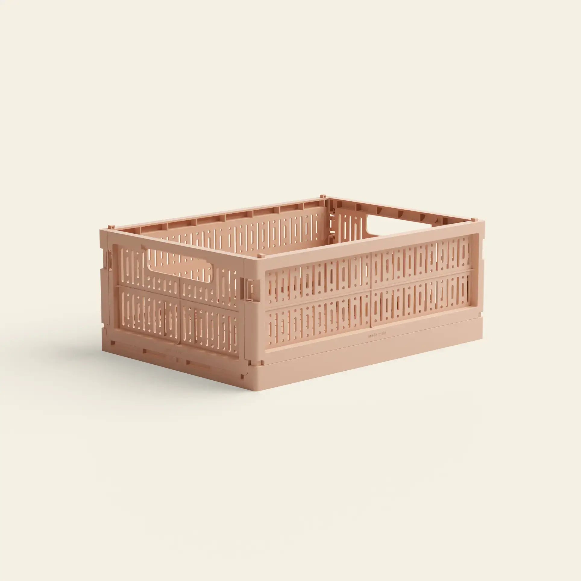 The Made Crate Midi by Made Crate is a light pink, rectangular recycled plastic crate with ventilation holes and built-in handles, offering eco-friendly stacking convenience on a plain, light background.