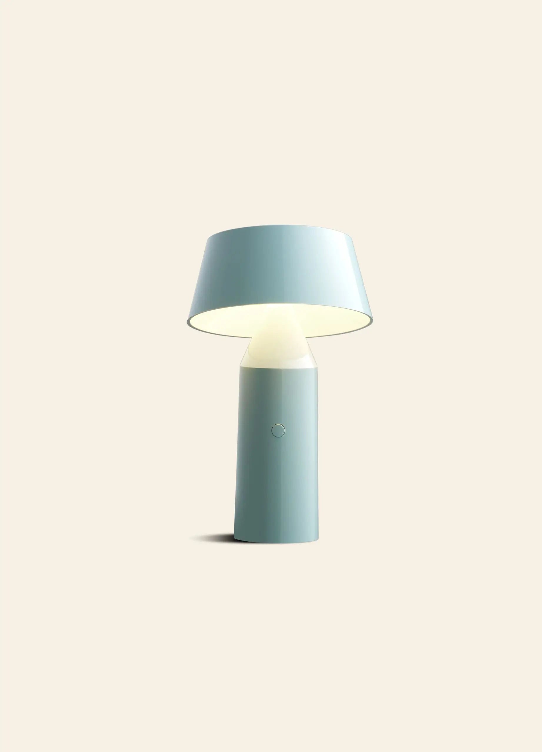 The Marset Bicoca Portable Table Lamp by Marset features a modern, minimalist blue design with a cylindrical base and wide conical shade, casting soft light—an ideal stylish accent for any contemporary space.