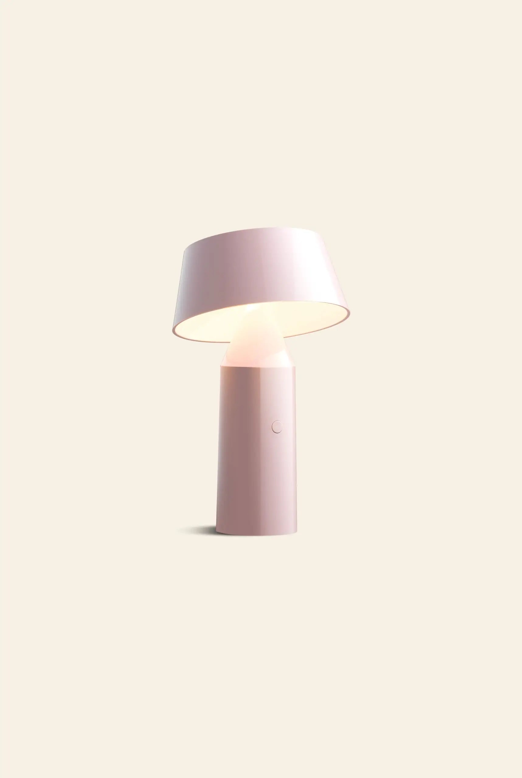 The Marset Bicoca Portable Table Lamp by Marset, featuring a modern minimalist design with a cylindrical base and a tilted wide lampshade, softly illuminates against a plain beige backdrop, bringing stylish flair to any space.