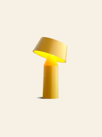 The Marset Bicoca Portable Table Lamp by Marset features a modern yellow design with a cylindrical base and tilted shade, casting warm light—ideal as a stylish table lamp for any space.