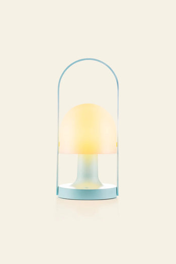 The Marset FollowMe Portable Table Lamp by Marset features a pale blue base, oak handle, and a dome-shaped soft yellow light, all set against a plain beige background.