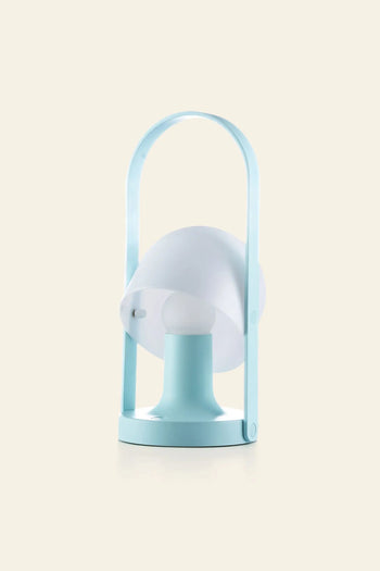 The Marset FollowMe Portable Table Lamp by Marset features a modern minimalist design with a light blue rechargeable body, circular base, frosted dome-shaped cover, and curved oak handle, shown against a plain light beige background.