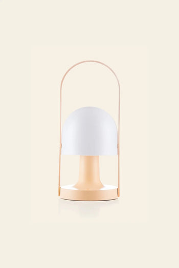 The Marset FollowMe Portable Table Lamp by Marset features a modern, minimalist design with a round white dome shade, light peach base, and matching arched handle, set against a plain cream background.