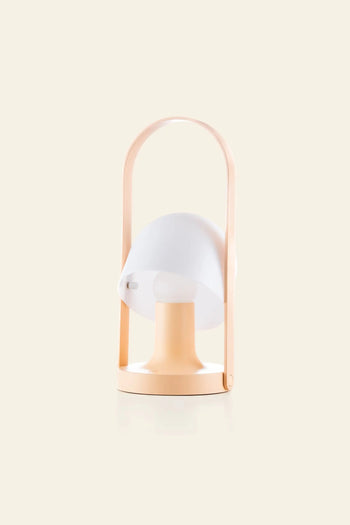 The Marset FollowMe Portable Table Lamp by Marset features a modern, minimalist design with a peach base, white mushroom-shaped shade, and arched oak handle, displayed against a plain light background.